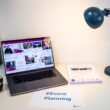A desk with an event flyer, a piece of paper with the hashtag #EventPlanning and a laptop showing a social media wall