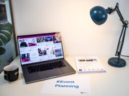 A desk with an event flyer, a piece of paper with the hashtag #EventPlanning and a laptop showing a social media wall