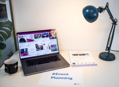 A desk with an event flyer, a piece of paper with the hashtag #EventPlanning and a laptop showing a social media wall