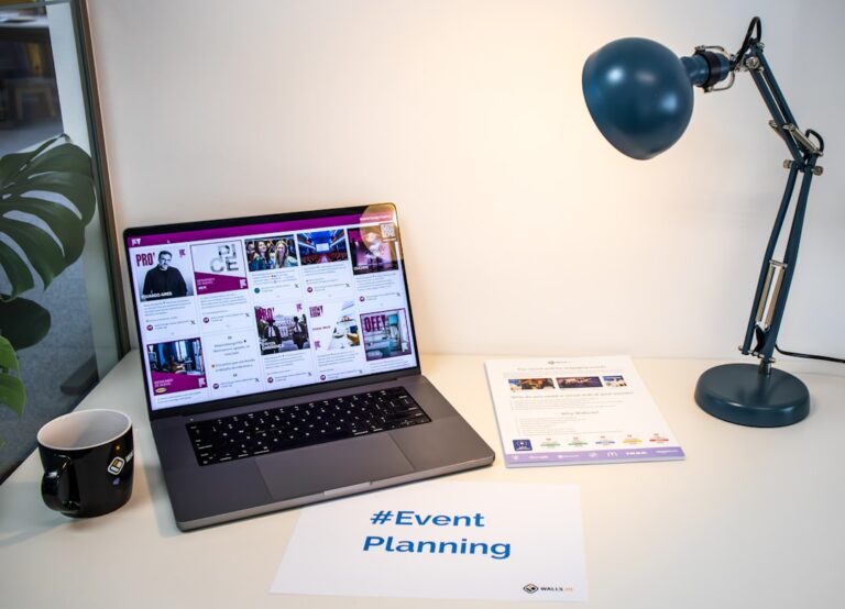 A desk with an event flyer, a piece of paper with the hashtag #EventPlanning and a laptop showing a social media wall
