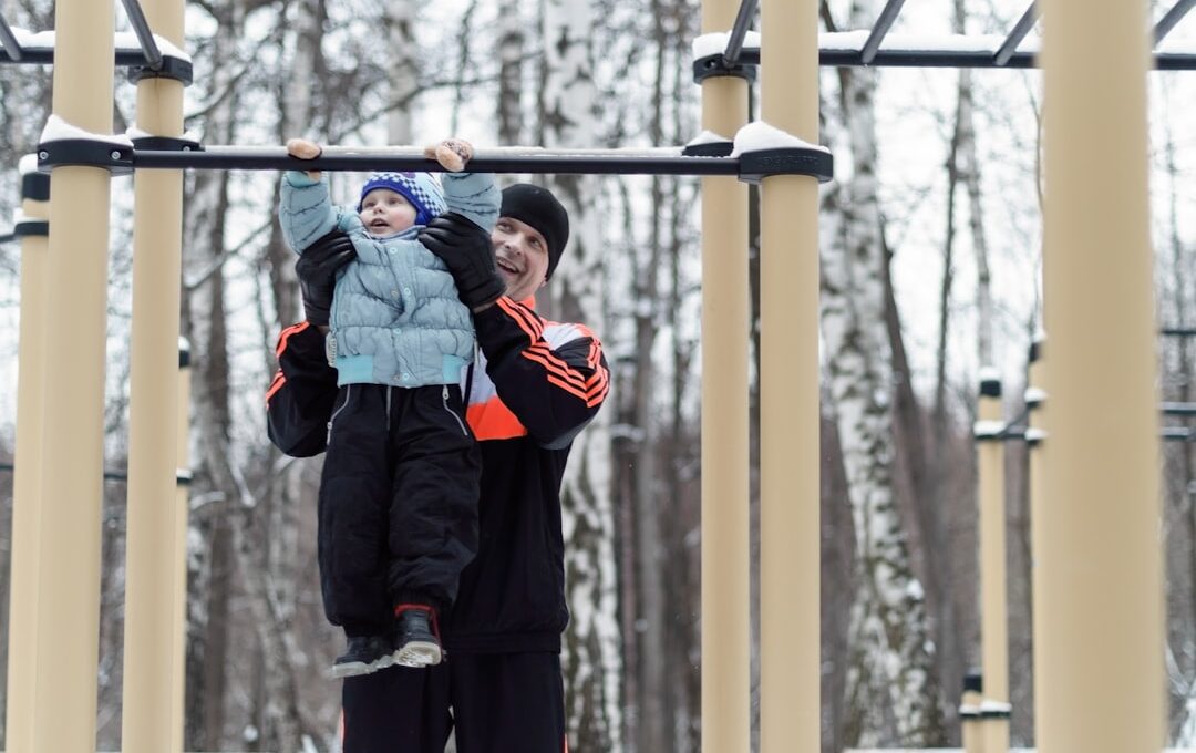 the father helping the boy on the horizontal bar in the park in winter