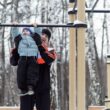the father helping the boy on the horizontal bar in the park in winter