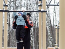 the father helping the boy on the horizontal bar in the park in winter