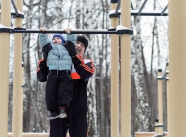 the father helping the boy on the horizontal bar in the park in winter