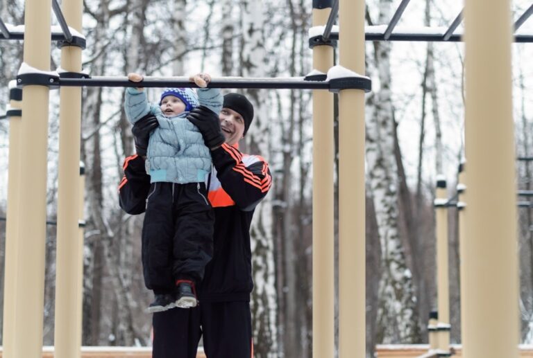 the father helping the boy on the horizontal bar in the park in winter