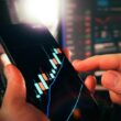 Cryptocurrency trading analysis mobile chart growth candlesticks. Close-up of hands analyzing bullish candlestick patterns on smartphone