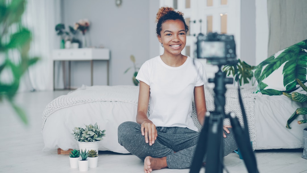 Female blogger is recording video for videolog looking at camera, smiling and talking emotionally sitting on bedroom floor at home. People, technology and social media concept.