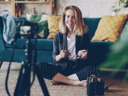 Make-up artist and blogger is recording video about face contouring for her vlog using professional camera. Young woman is holding brush and cosmetics kit and speaking.