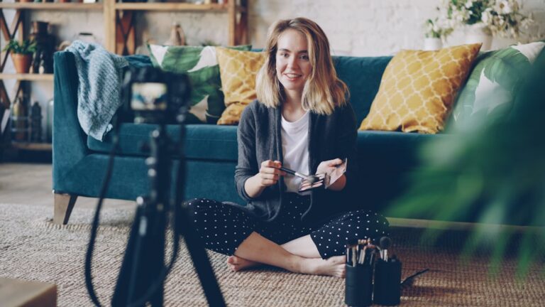 Make-up artist and blogger is recording video about face contouring for her vlog using professional camera. Young woman is holding brush and cosmetics kit and speaking.