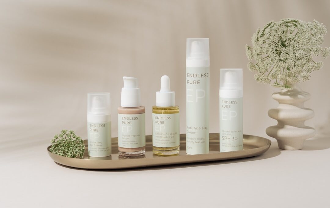 A beautifully arranged display of elegant skincare products on a marble tray against a soft, beige backdrop. The collection includes various bottles and jars, showcasing a range of serums, creams, and SPF protection. The minimalist design and soft pastel colors create a clean, luxurious aesthetic. A delicate floral arrangement in a textured vase adds a natural touch to the composition, enhancing the serene and sophisticated vibe.