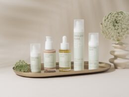 A beautifully arranged display of elegant skincare products on a marble tray against a soft, beige backdrop. The collection includes various bottles and jars, showcasing a range of serums, creams, and SPF protection. The minimalist design and soft pastel colors create a clean, luxurious aesthetic. A delicate floral arrangement in a textured vase adds a natural touch to the composition, enhancing the serene and sophisticated vibe.