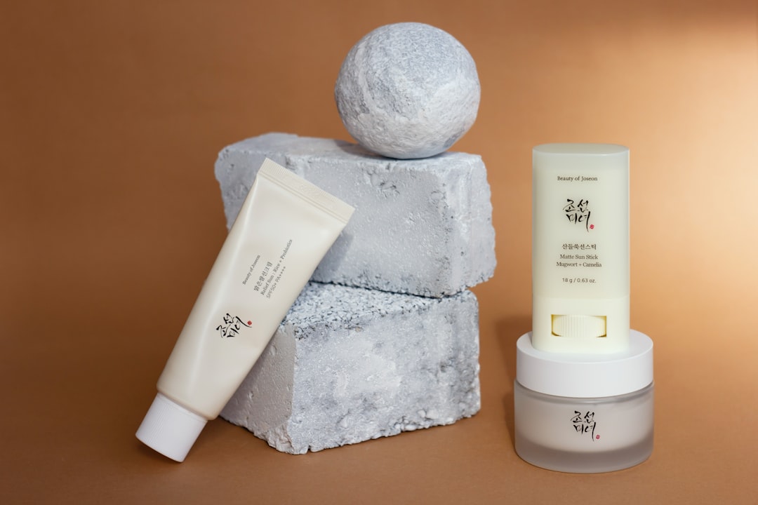 Two different sunscreens and a moisturizer from one K-brand make up a modern minimalist composition with rough pieces of painted concrete on a warm glowing background.