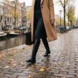 Vrouw loopt in de herfst over de keien langs een gracht in hoge zwarte leren laarzen over een donkere jeans