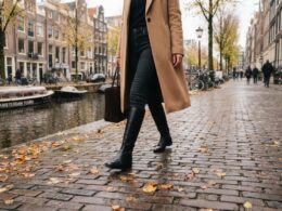 Vrouw loopt in de herfst over de keien langs een gracht in hoge zwarte leren laarzen over een donkere jeans
