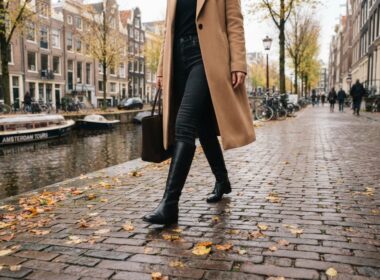 Vrouw loopt in de herfst over de keien langs een gracht in hoge zwarte leren laarzen over een donkere jeans